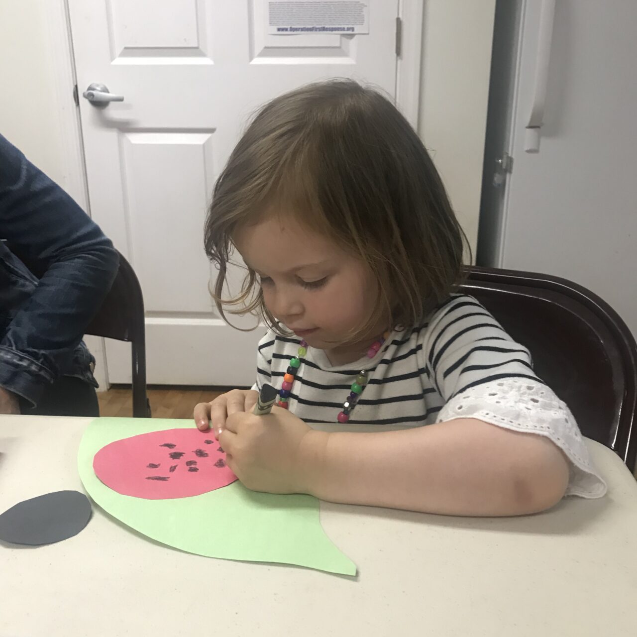 A little girl sitting at the table with a watermelon cut out.