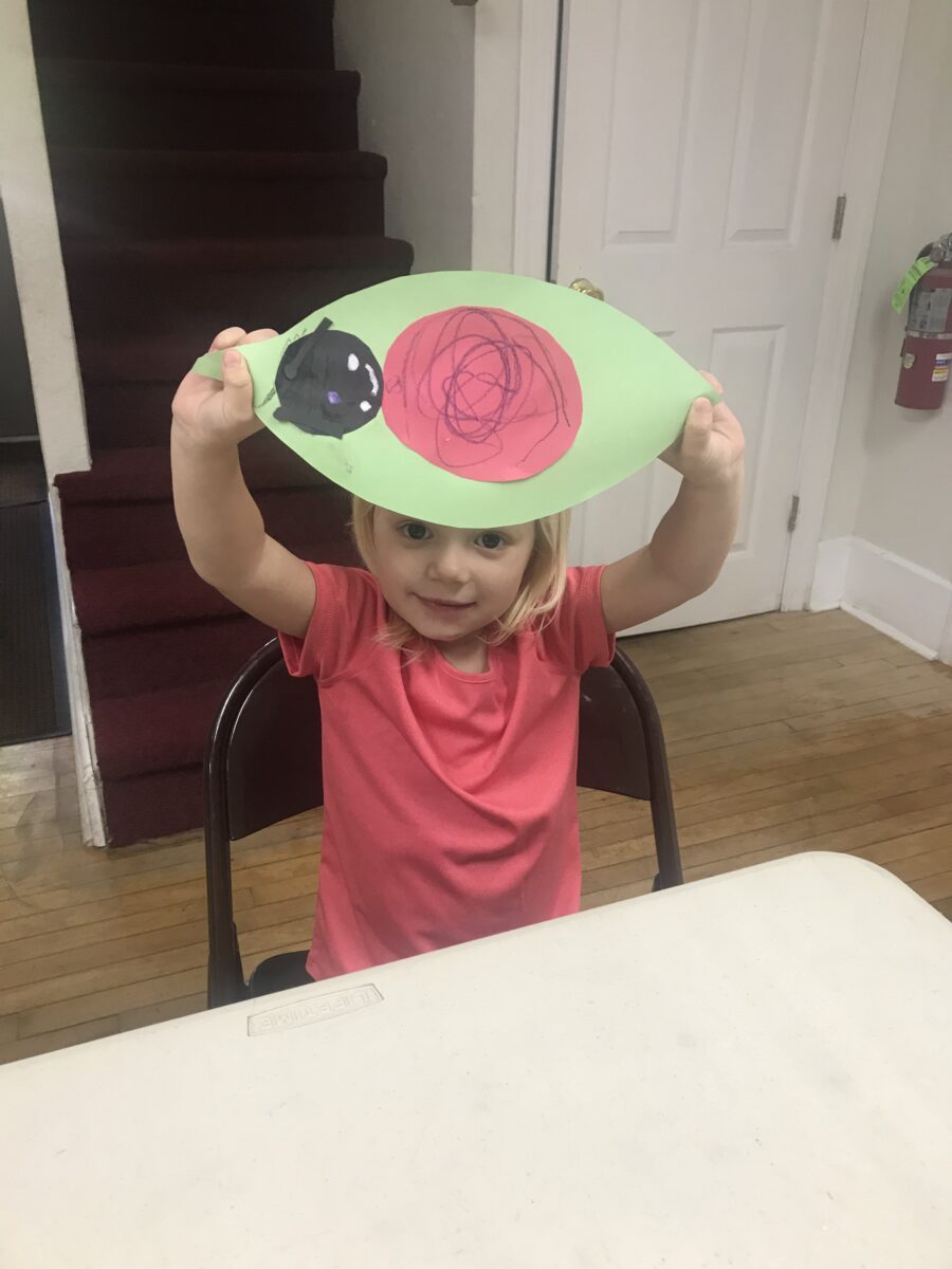 A little girl holding up an apple on top of her head.