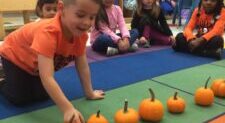 Here's a concise alt tag for the image: `Preschooler counting mini pumpkins`