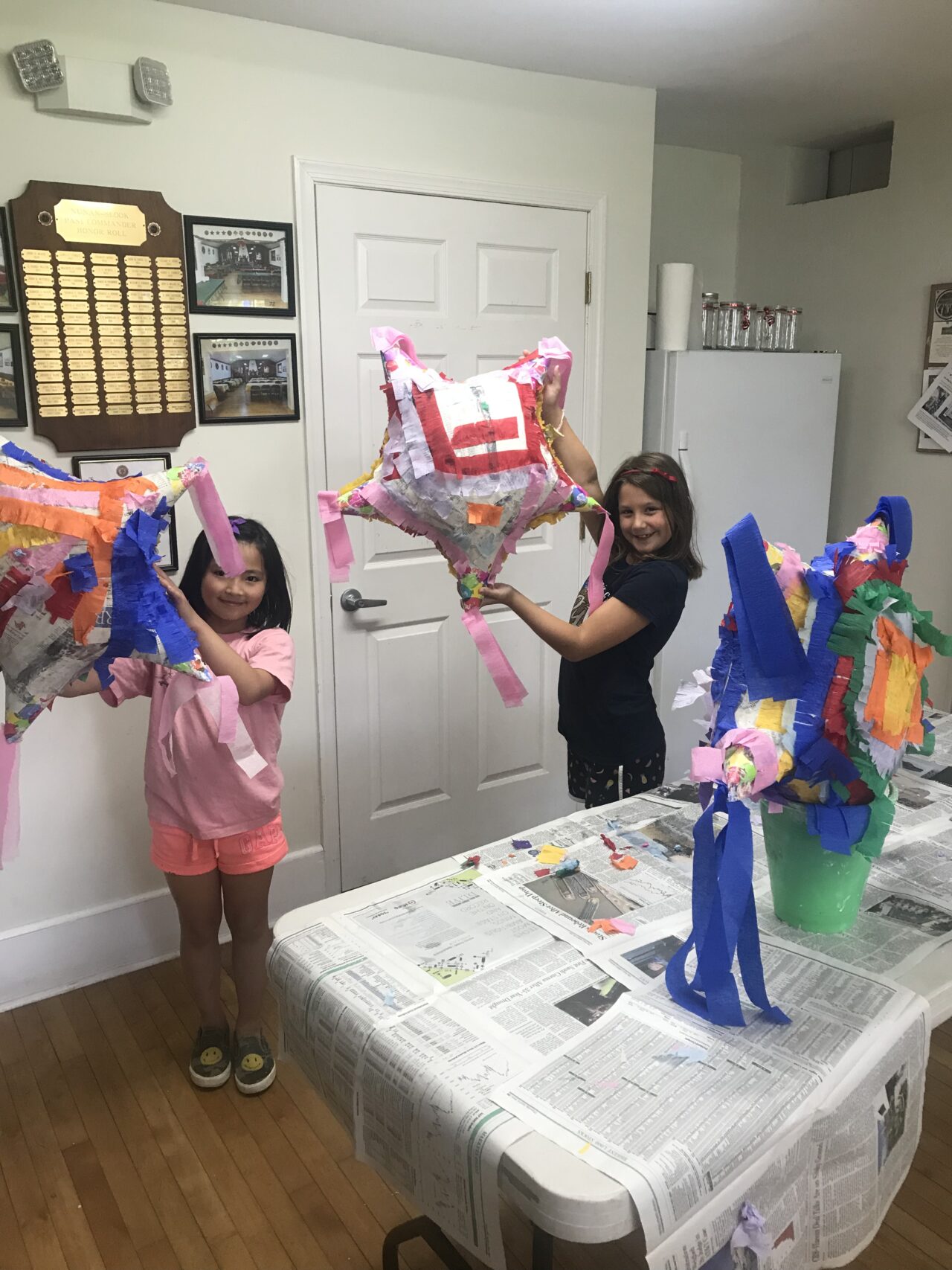 Two girls holding up balloons in front of a table.