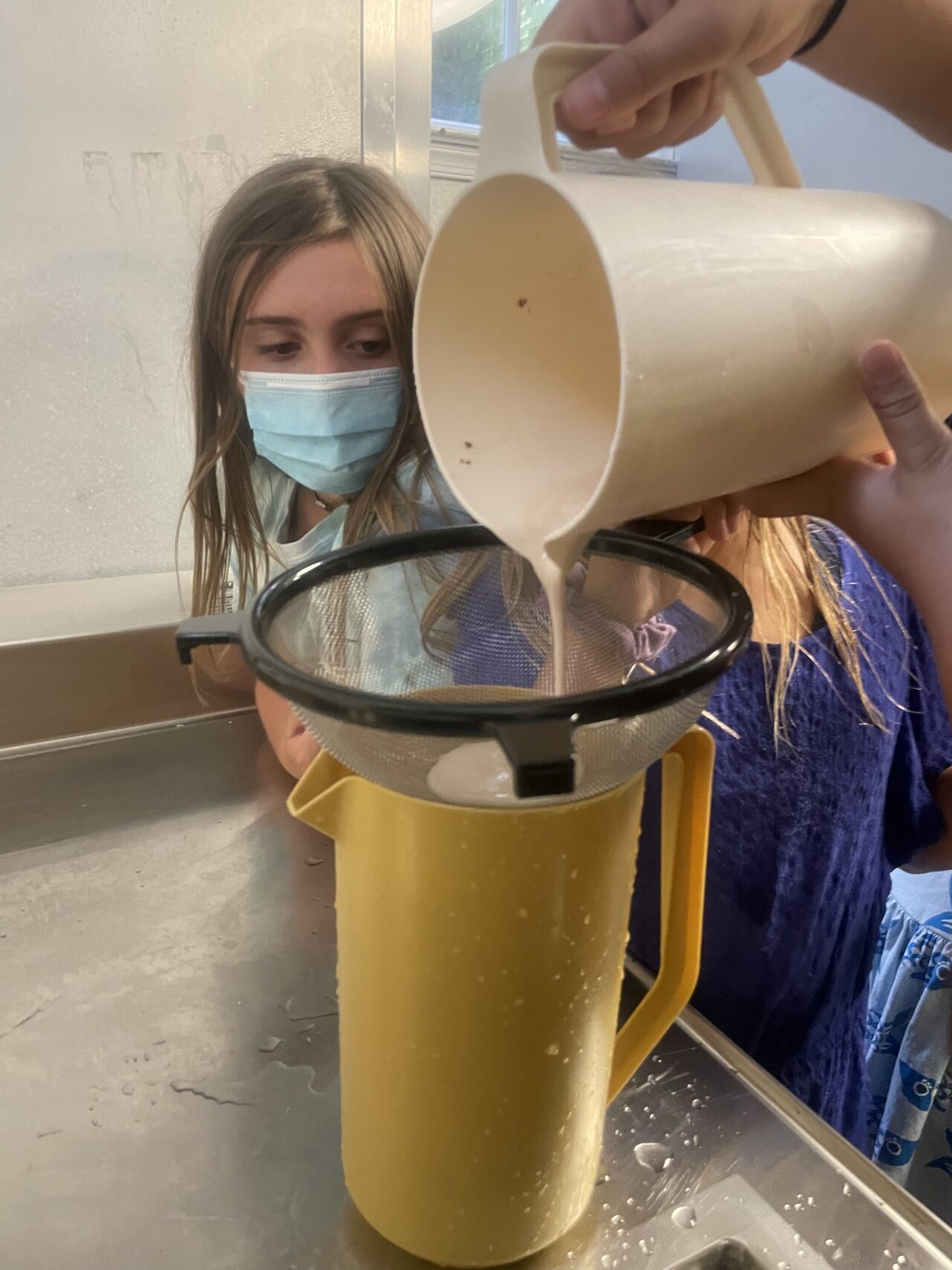 A girl in a mask is pouring something into a cup.