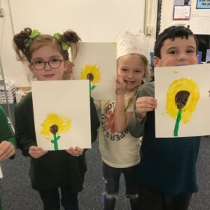 Here's an alt tag for the image: Preschool children proudly display sunflower paintings.