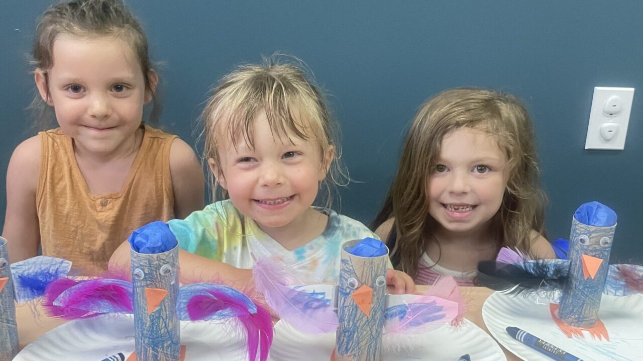 Three children sitting at a table with plates of food.