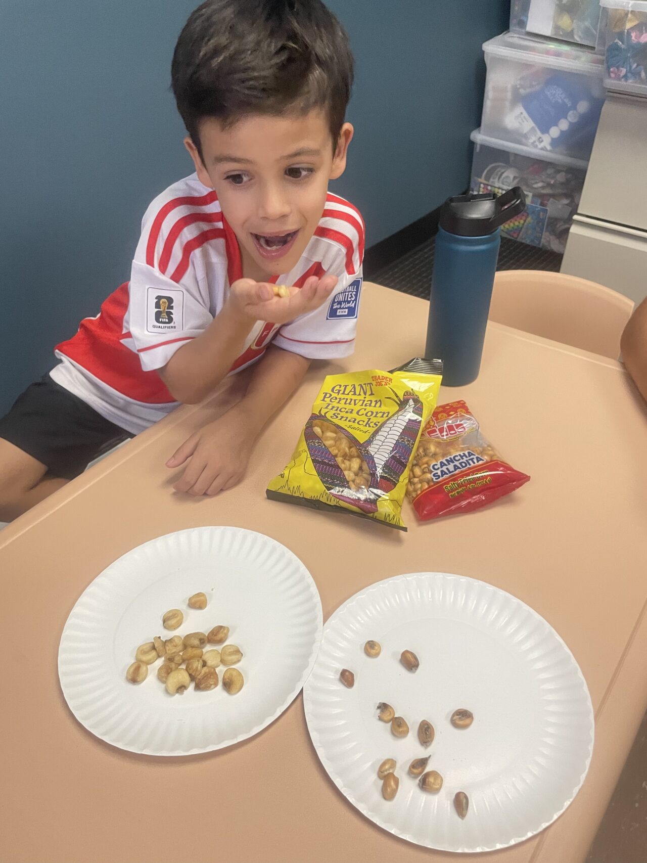 A boy sitting at the table with two paper plates of nuts.