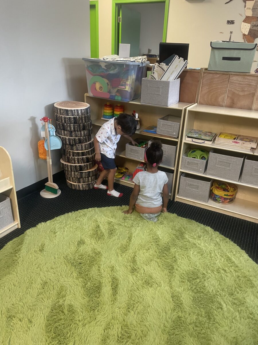 Two children are playing in a room with green carpet.